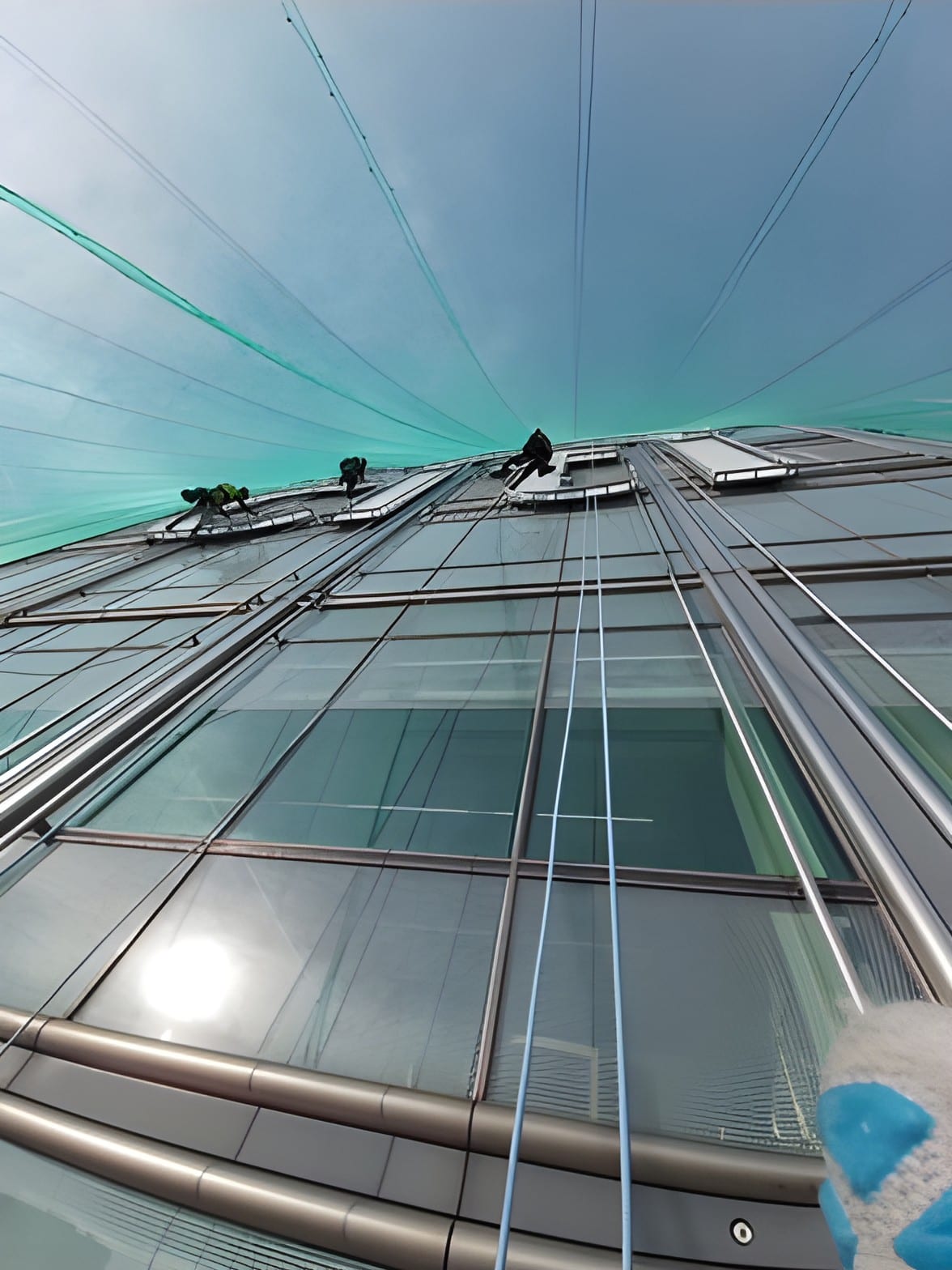 Two IRATA rope access technicians abseiling down a glass office tower beneath safety netting
